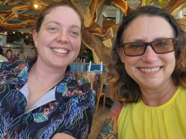 Dr. April Haas, smiling in a Hawaiian shirt, and Birdie Ganz, smiling with glasses and a yellow dress, at a restaurant in Honolulu at DADD 2024.
